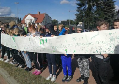 Długi plakat trzymają uczniowie, w tle budynki